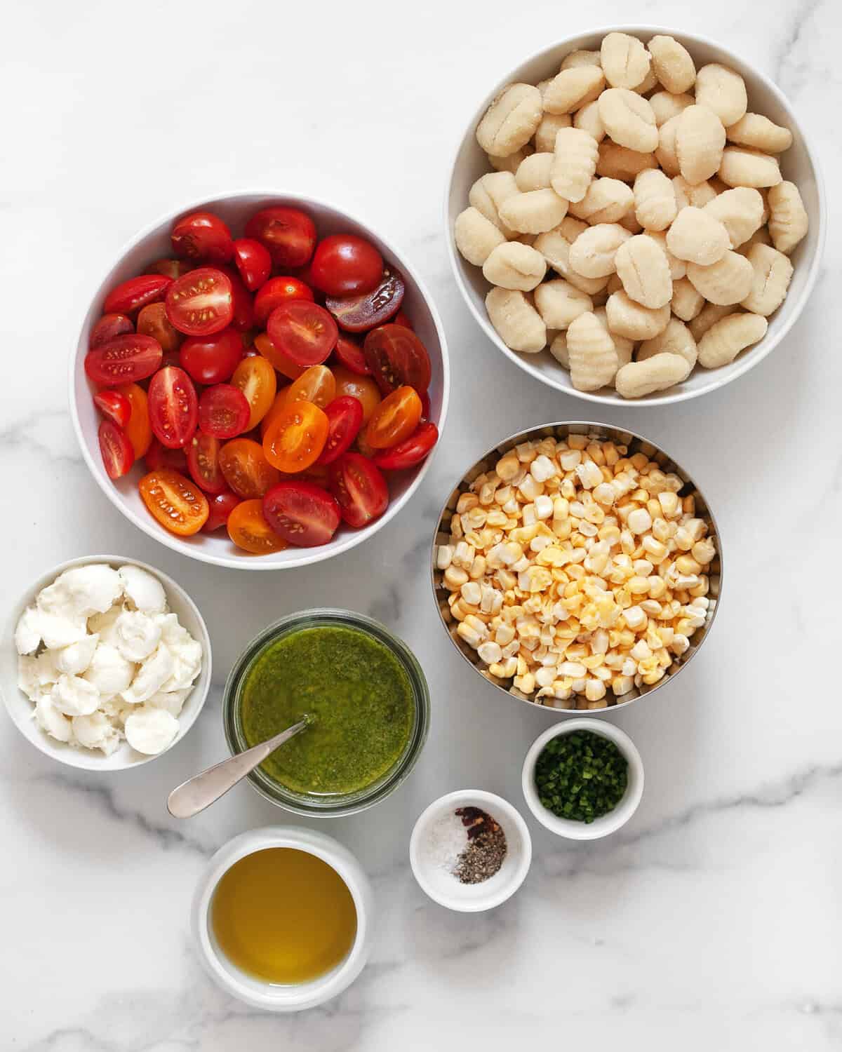 Ingredients including gnocchi, tomatoes, corn, pesto, mozzarella, olive oil, chives, red pepepr flakes, salt and pepper.
