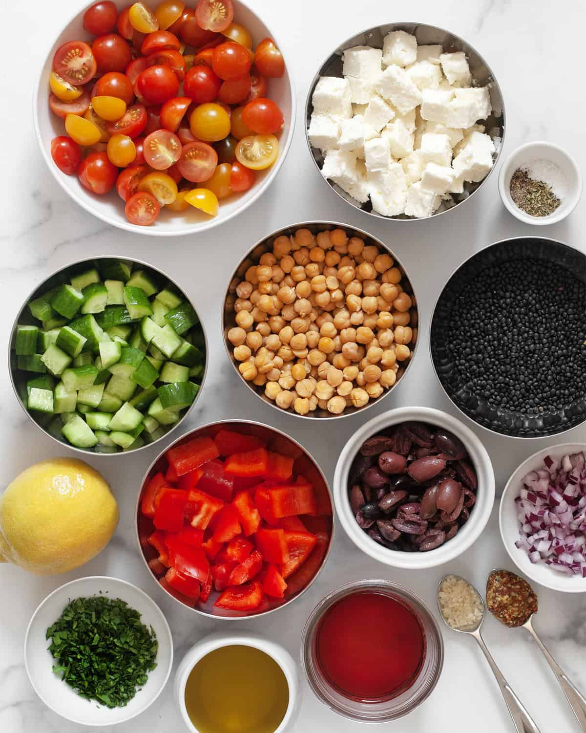 Ingredients including black lentils, tomatoes, cucumbers, olives, bell peppers, fetam red onions, lemon, parsley, chickpeas, feta, red wine vinegar, salt, pepper and olive oil.
