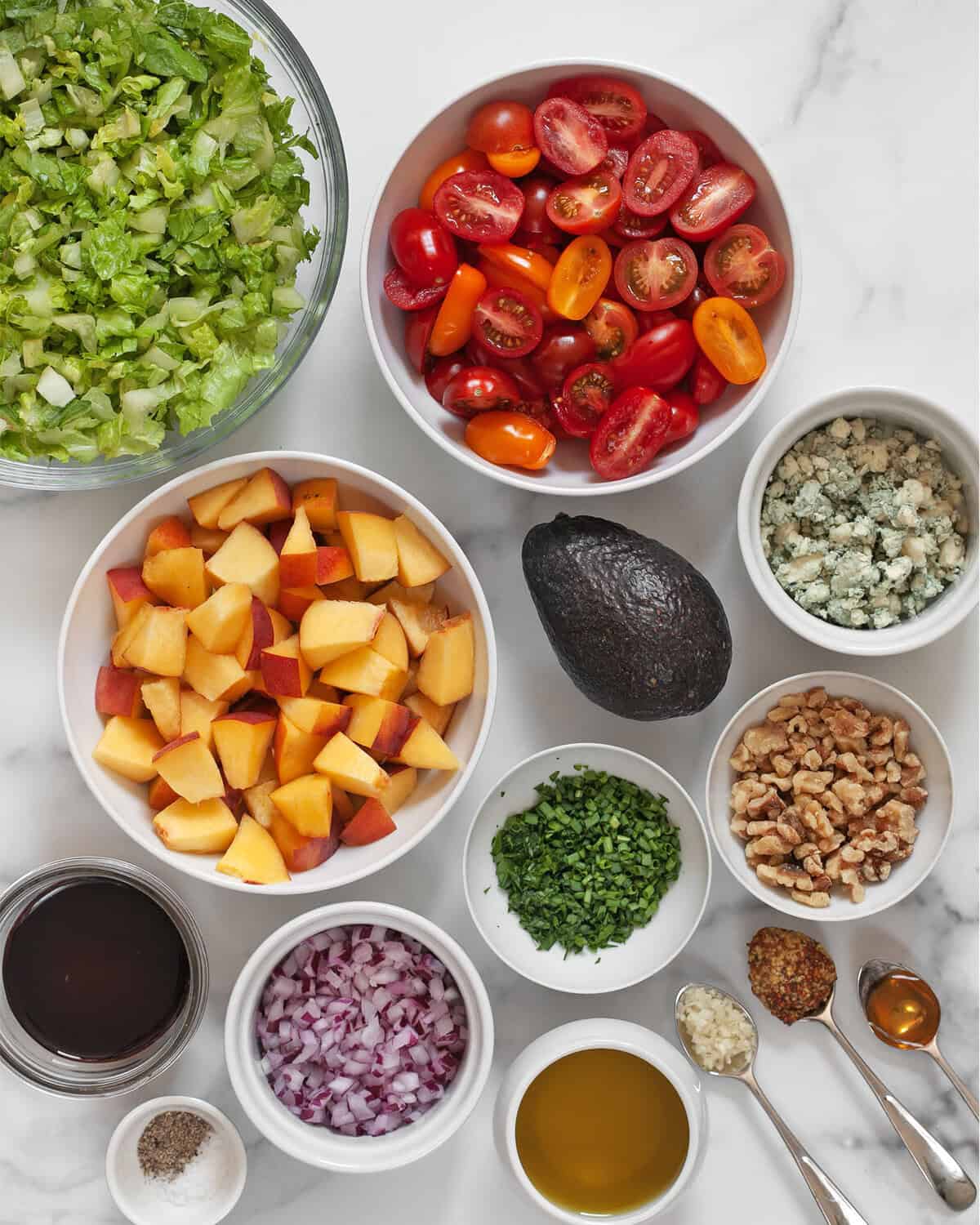 Ingredients including peaches, tomatoes, avovado, romaine, walnuts, blue cheese, fresh herbs, red onions, mustard, garlic, olive oil, salt pepper and balsamic vinegar.