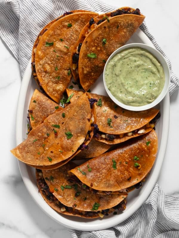 Crispy corn tacos on an oval platter with avocado crema.