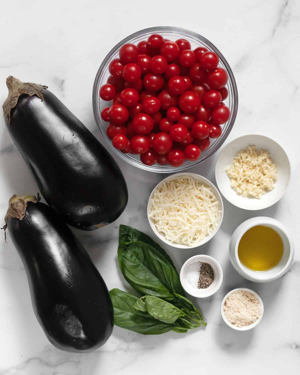 Ingredients including eggplants, cherry tomatoes, basil, shredded cheese, grated parmesan, garlic, olive oil, salt and pepper.