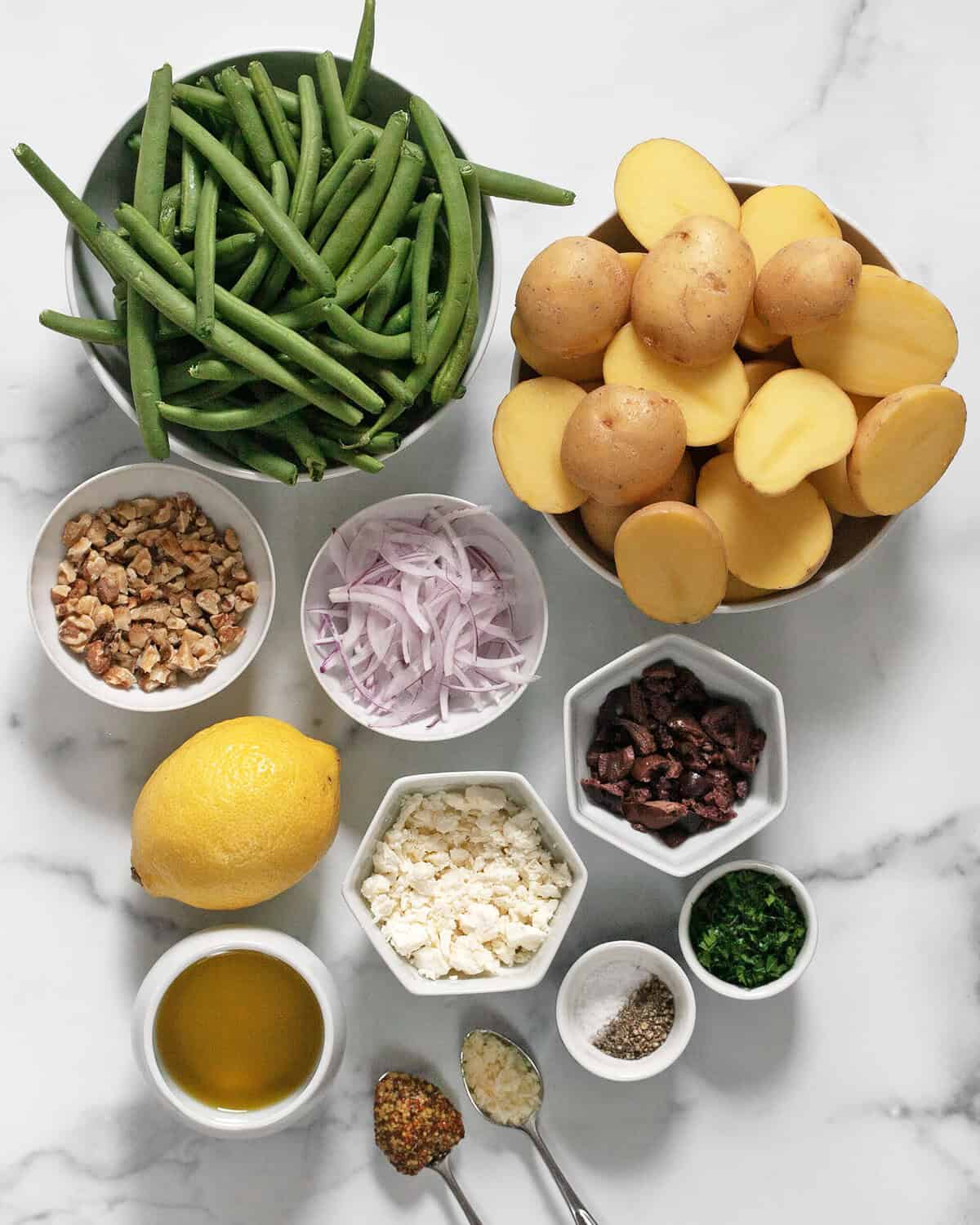 Ingredients including potatoes, green beans, red onions, olives, lemon, feta, olive oil, parsley, salt and pepper.