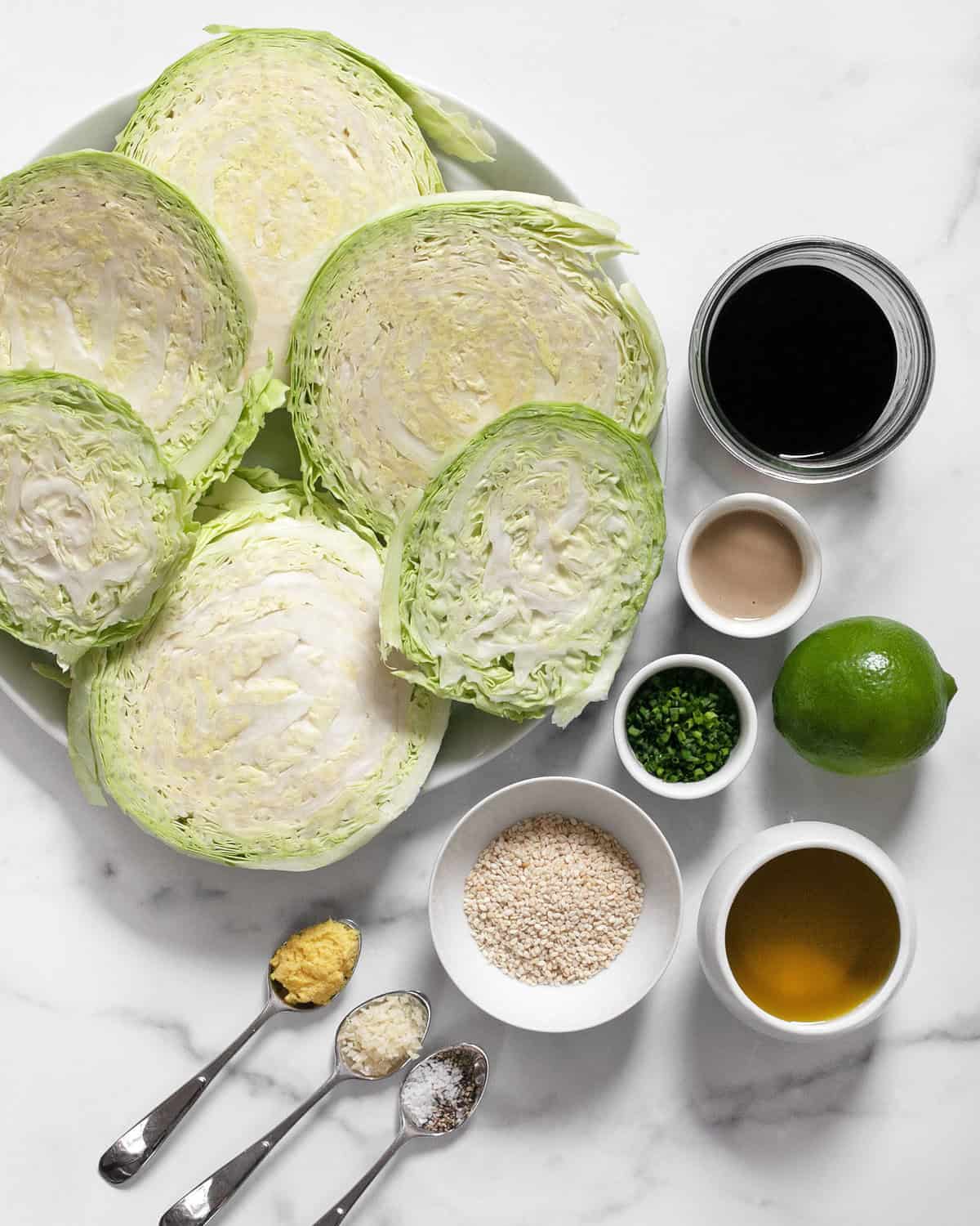 Ingredients including sliced cabbage, soy sauce, tahini, fresh herbs, lime, olive oil, sesame seeds, ginger garlic, salt and pepper.