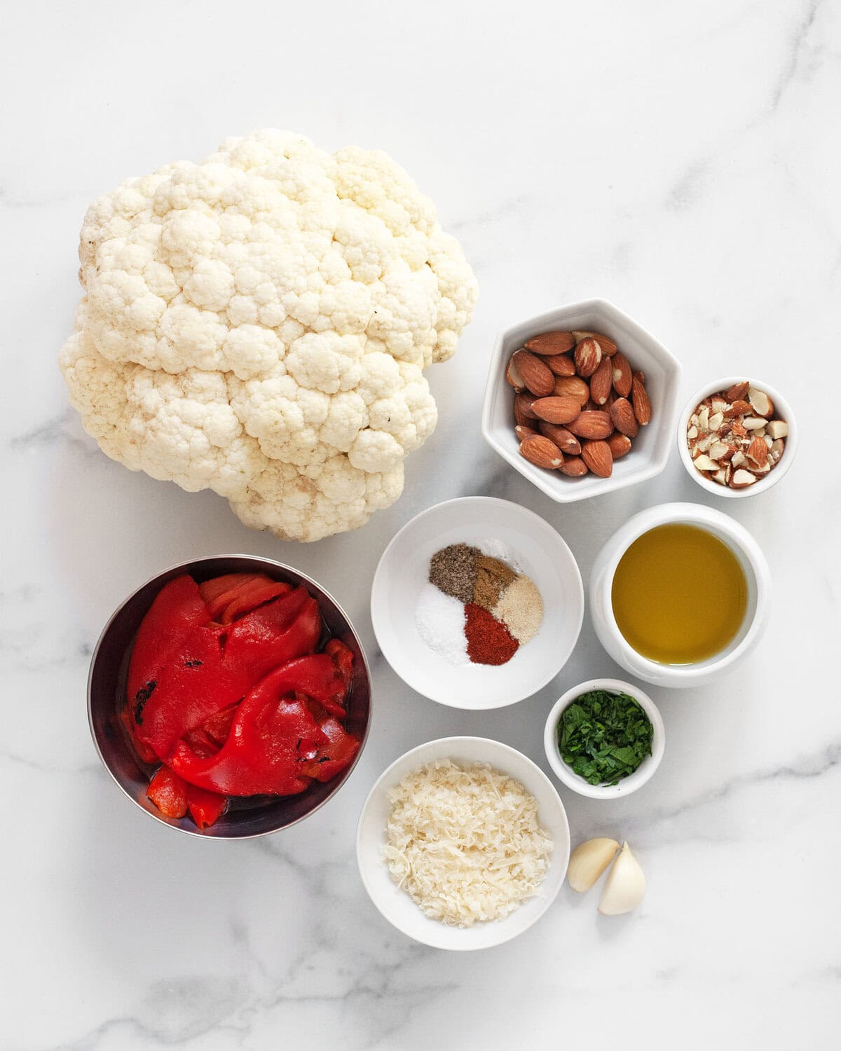 Ingredients including cauliflower head, olive oil. seasonings, parsley. garlic, parmesan, almonds and roasted red peppers.