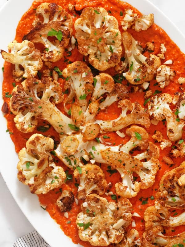 Roasted cauliflower steaks with roasted red pesto on a serving platter.