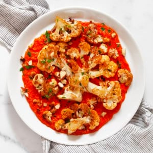 Roasted cauliflower steaks with roasted red pesto on a plate.