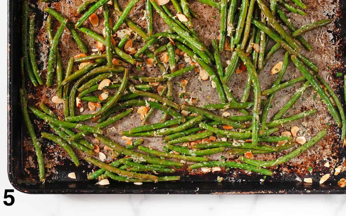 Roasted green beans tossed with lemon zest, toasted almonds and fresh herbs on a baking sheet.