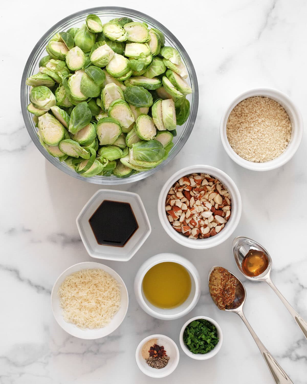 Ingredients including brussels sprouts, almonds, breadcrumbs, balsamic vinegar, olive oil, honey, seasonings, parmesan and parsley.