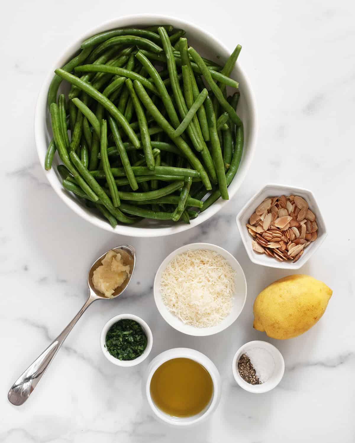 Ingredients including green beans, almonds, parmesan, garlic paste, lemon, olive oil, parsley, salt and pepper.