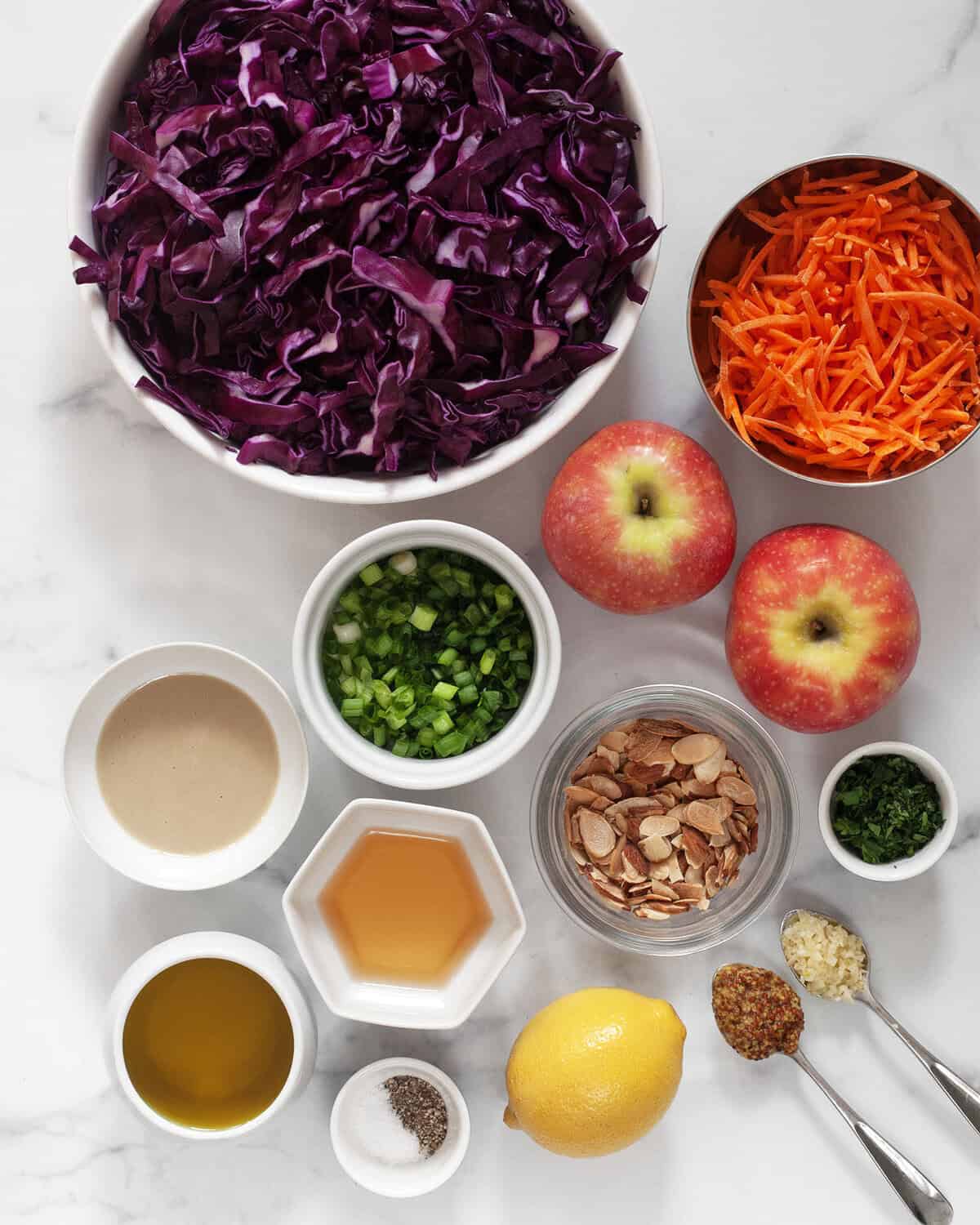 Ingredients including red cabbage, apples, carrots, almonds, scallions, parsley, tahini, apple cider vinegar, garlic, mustard and lemon.