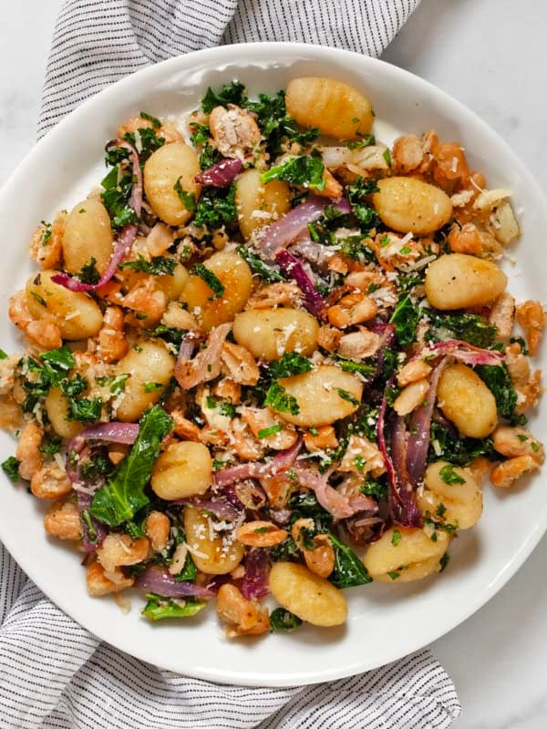 Sheet pan gnocchi with white beans, kale and red onions on a plate.