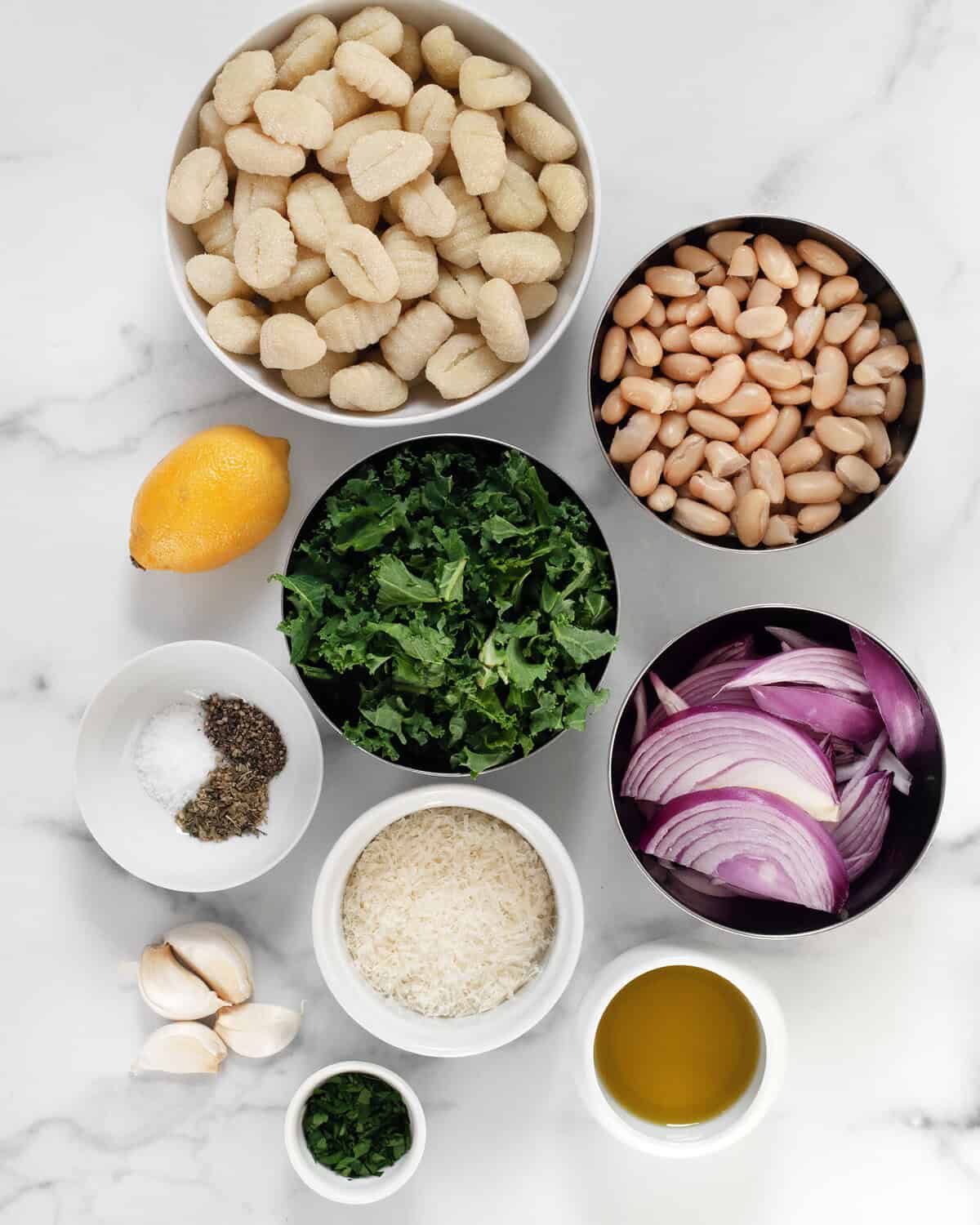 Ingredients including gnocchi, kale, cannellini beans, red onions, parmesan, parsley, lemon, olive oil and seasonings.