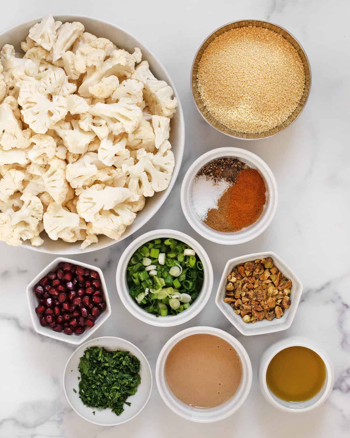 Ingredients including cauliflower, couscous, tahini, spices, scallions, parsley, pomegranate seeds, pistachios and olive oil.