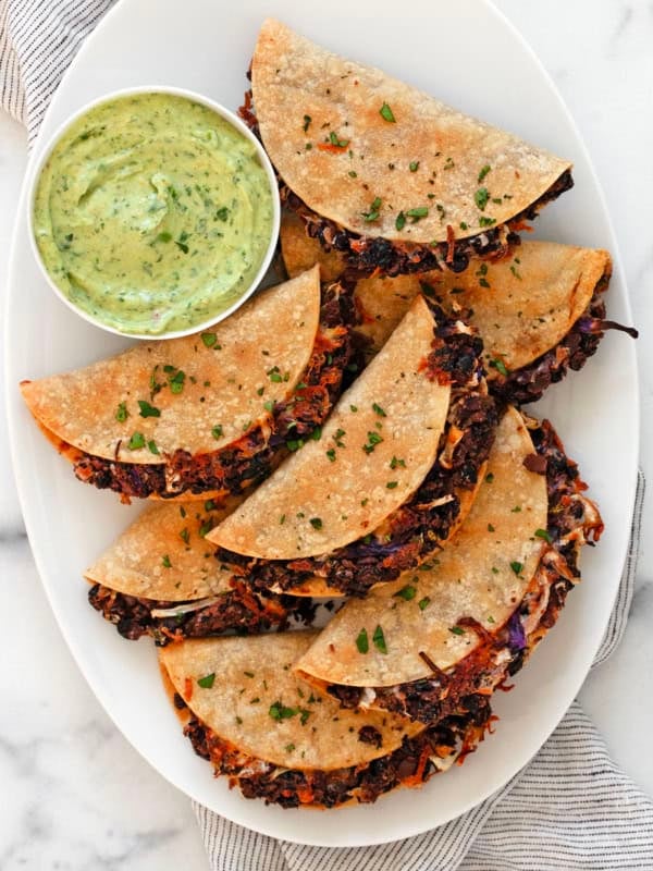 Crispy black beans tacos on a serving plate with avocado sauce in a small bowl.