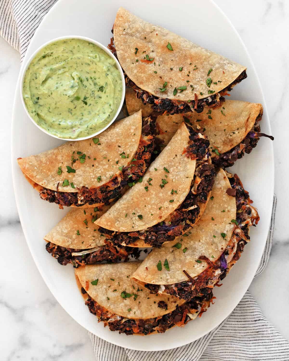 Crispy black beans tacos on a serving plate with avocado sauce in a small bowl.