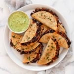 Crispy black beans tacos on a serving plate with avocado sauce in a small bowl.