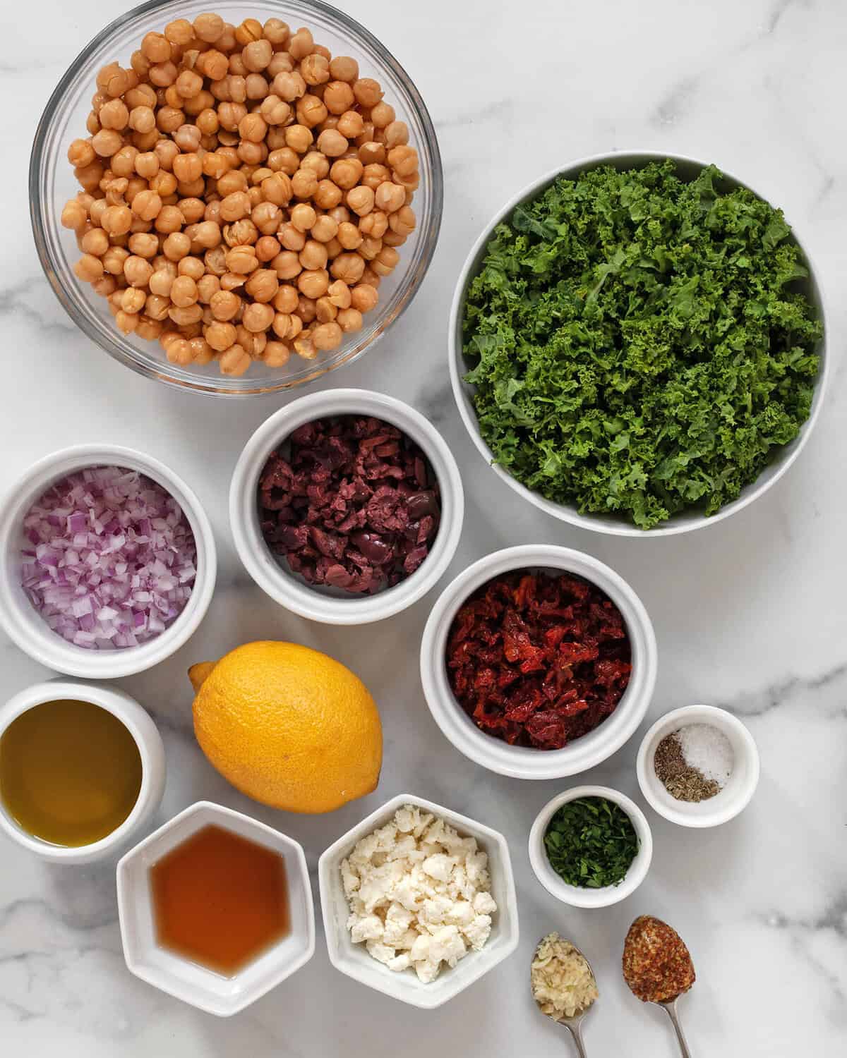 Ingredients including kale, chickpeas, red onions, sun dried tomatoes, kalamata olives, parsley, lemon, feta, red wine vinegar, olive oil, mustard, garlic, salt and pepper.