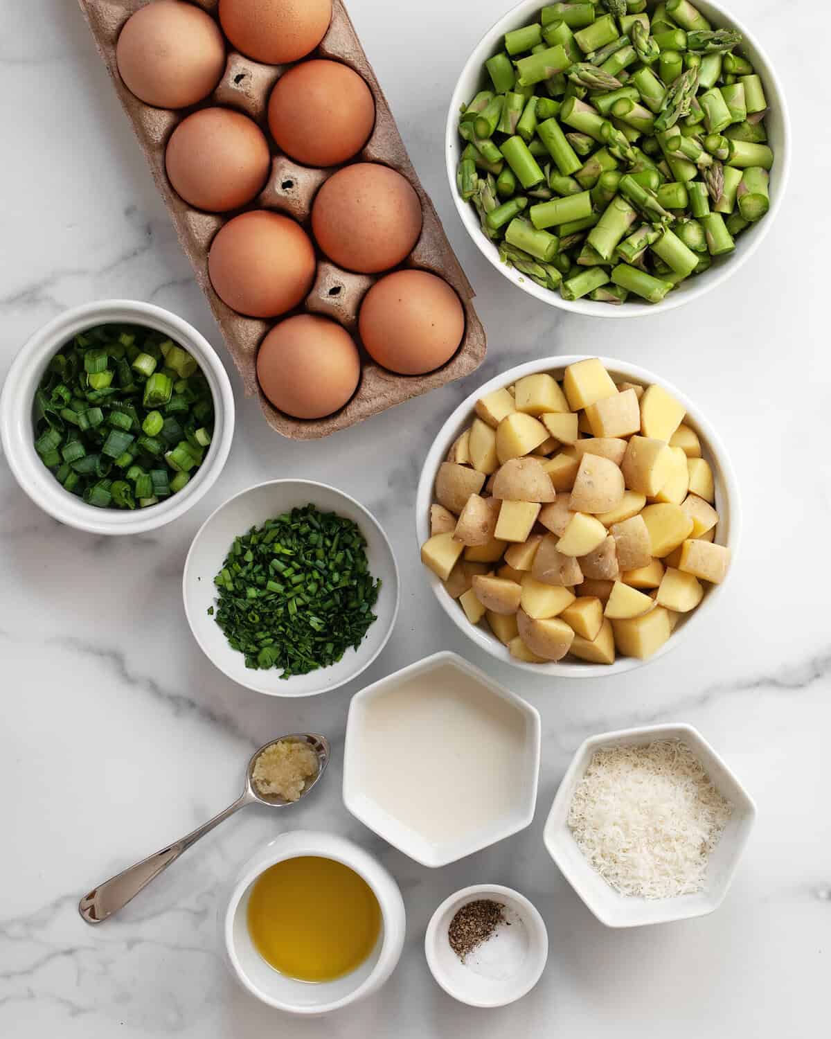 Ingredients including eggs, asparagus, potatoes, chives, parsley, milk, parmesan, garlic, scallions, olive oil, salt and pepper.