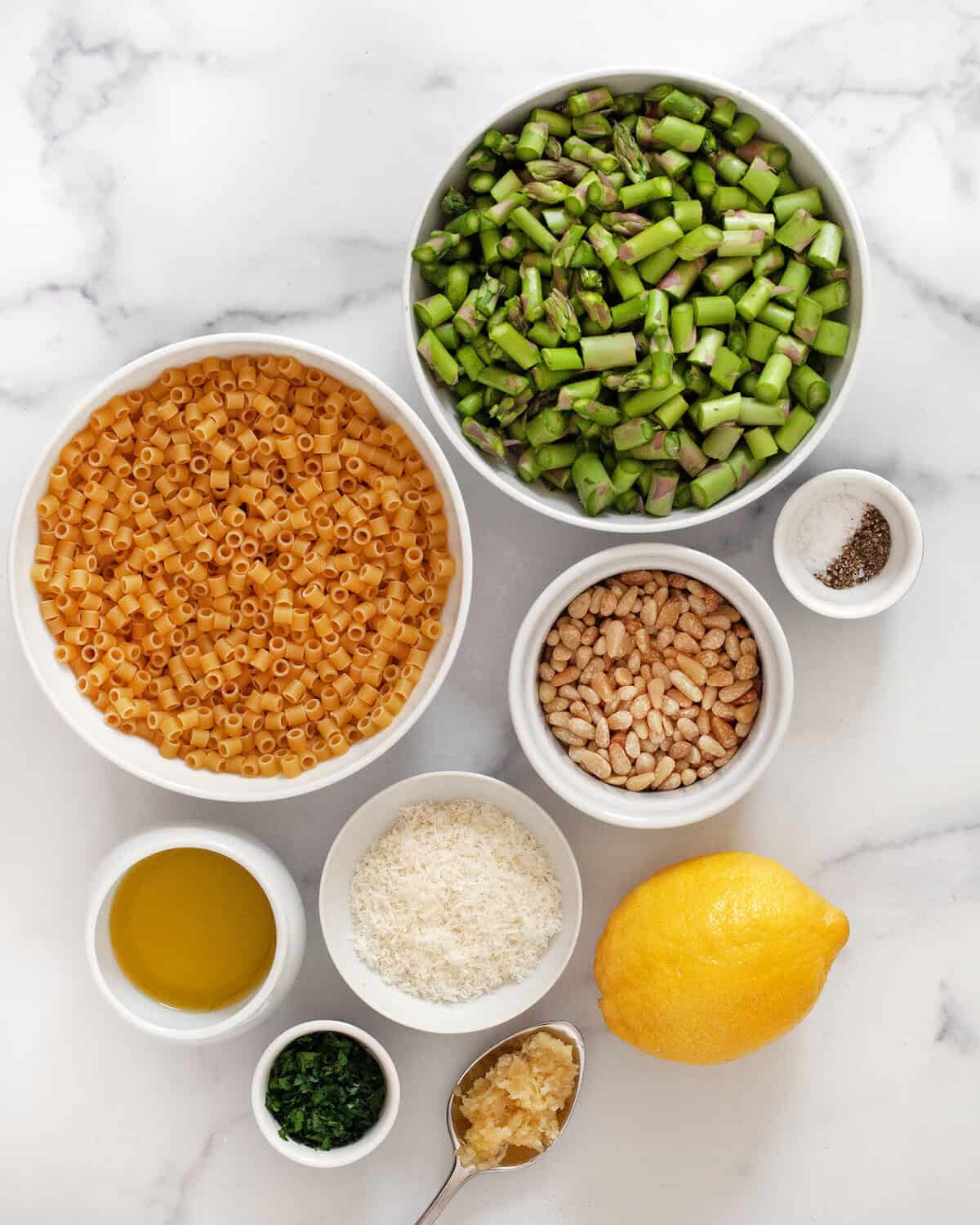 Ingredients including ditalini, sliced asparagus, pine nuts, grated parmesan, lemon, olive oil, parsley, minced garlic, kosher salt and black pepper.