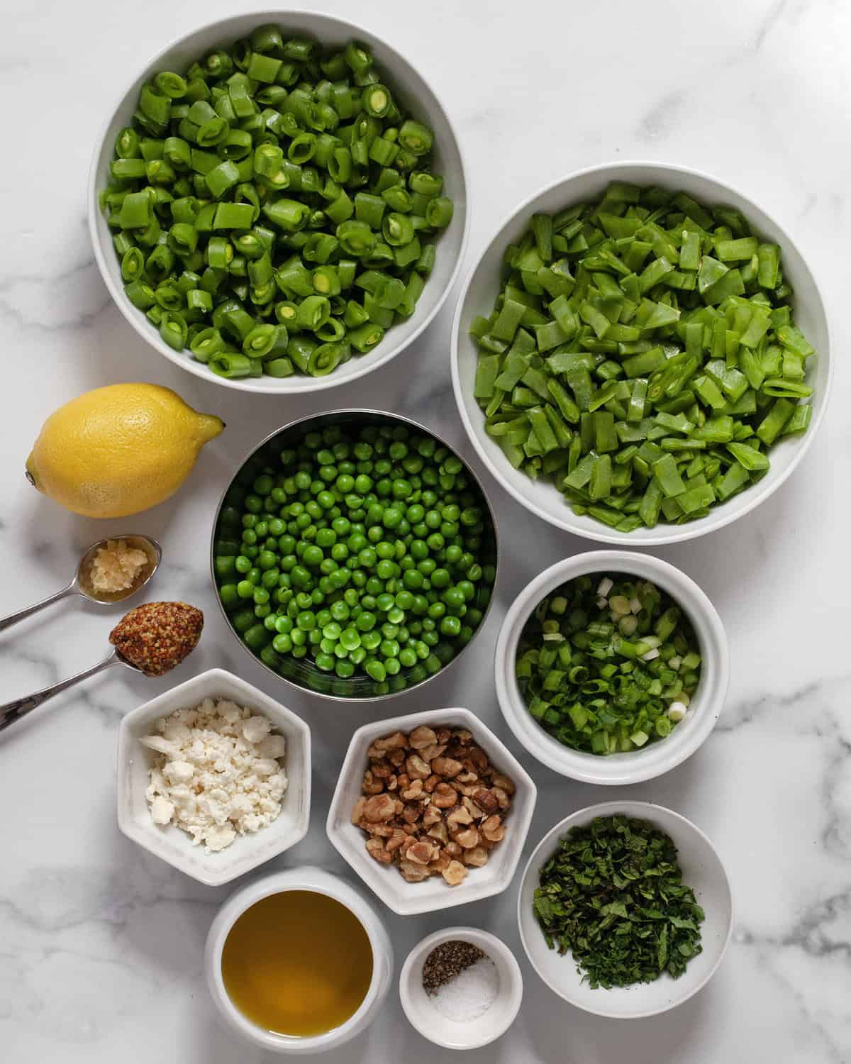 Ingredients including chopped snap peas and snow peas, shelled peas, walnuts, scallions, feta, lemon, garlic, mustard, olive oil, salt, pepper, parsley and mint.