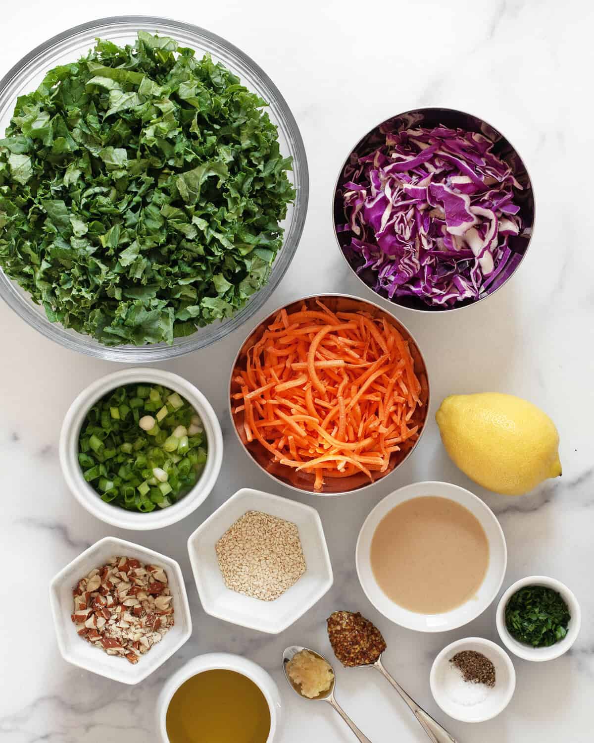 Ingredients including kale, cabbage, carrots, almonds, sesame seeds, tahini, lemon, olive oil, garlic, mustard, salt and pepper.