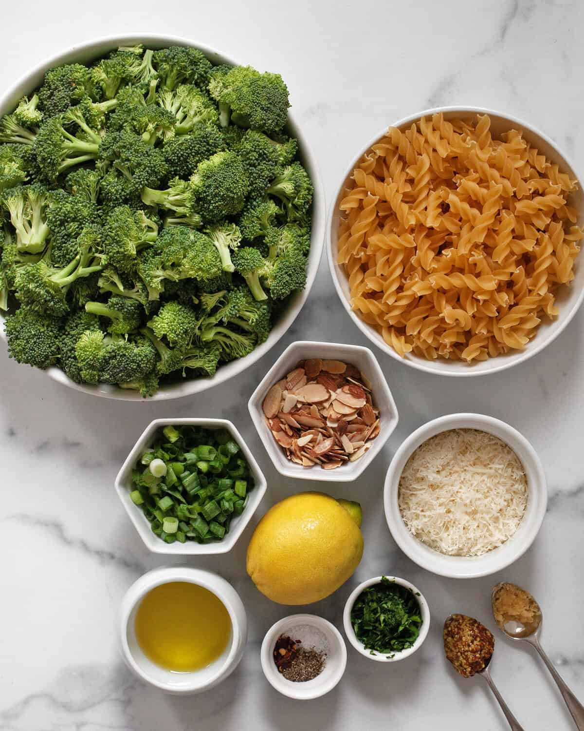 Ingredients including broccoli, fusilli, sliced almonds, scallions, parmesan, lemon, parsley, garlic, mustard, olive oil, red pepper flakes, salt and pepper.