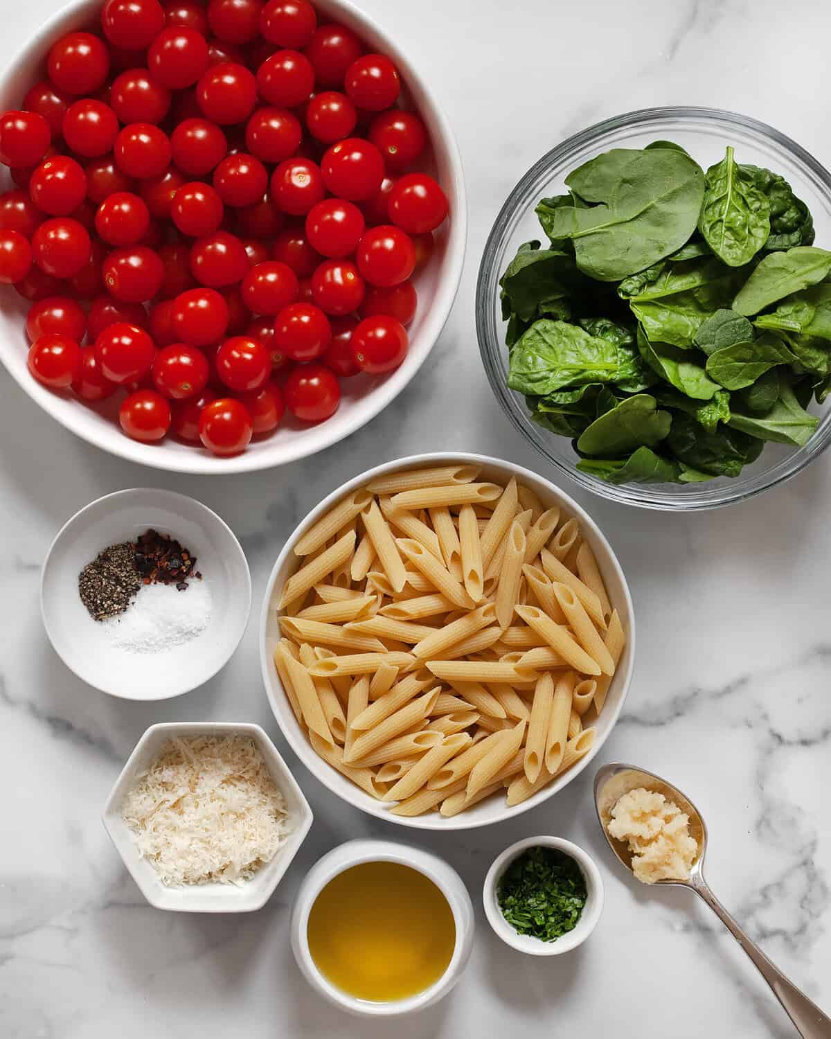 Ingredients including cherry tomatoes, penne, baby spinach, dried seasonings, garlic, olive oil, parmesan, garlic and fresh herbs