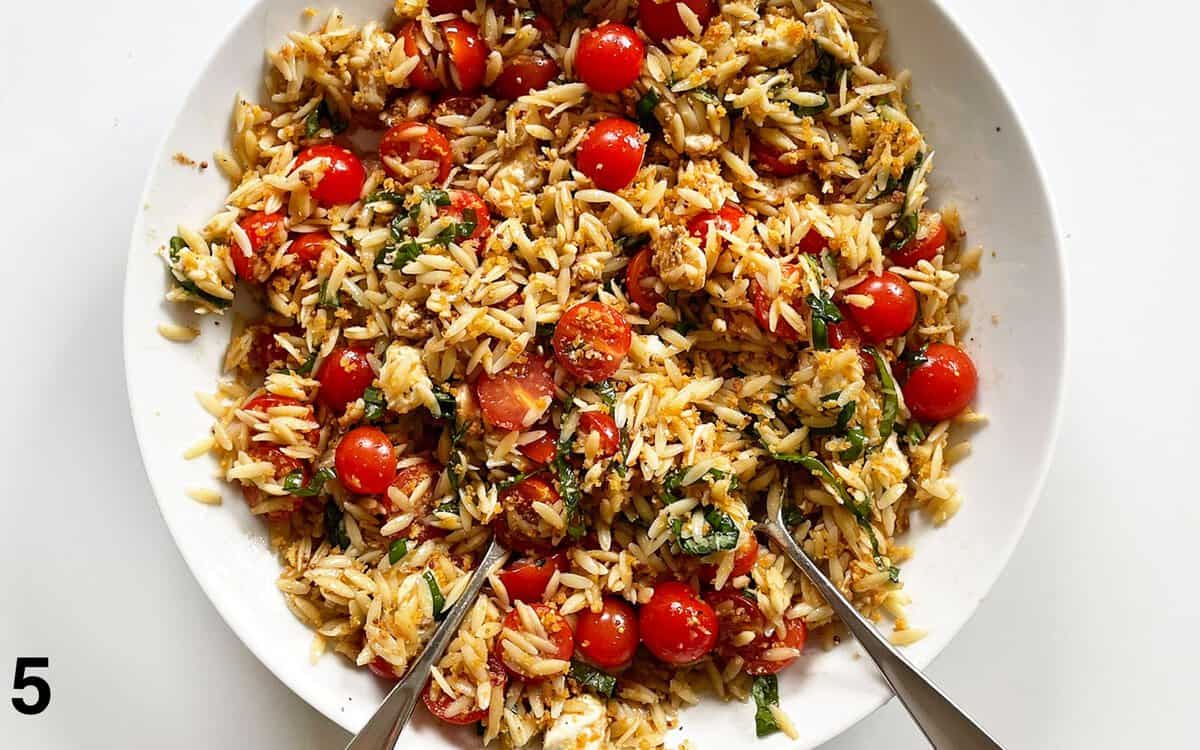 Breadcrumbs stirred into pasta salad in a large bowl.