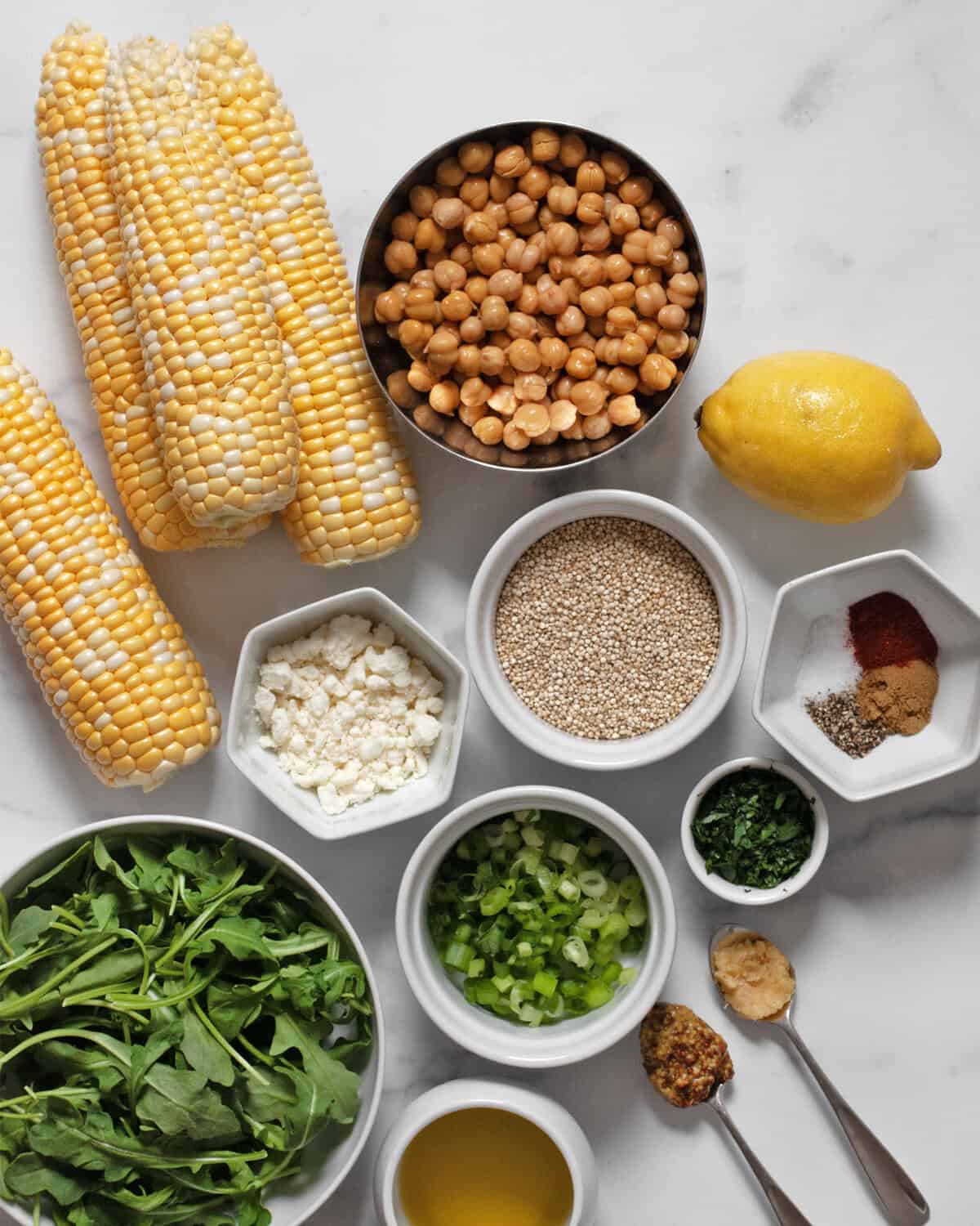 Ingredients including corn, chickpeas, arugula, quinoa, feta, parsley, lemon, garlic, mustard, spices and olive oil.