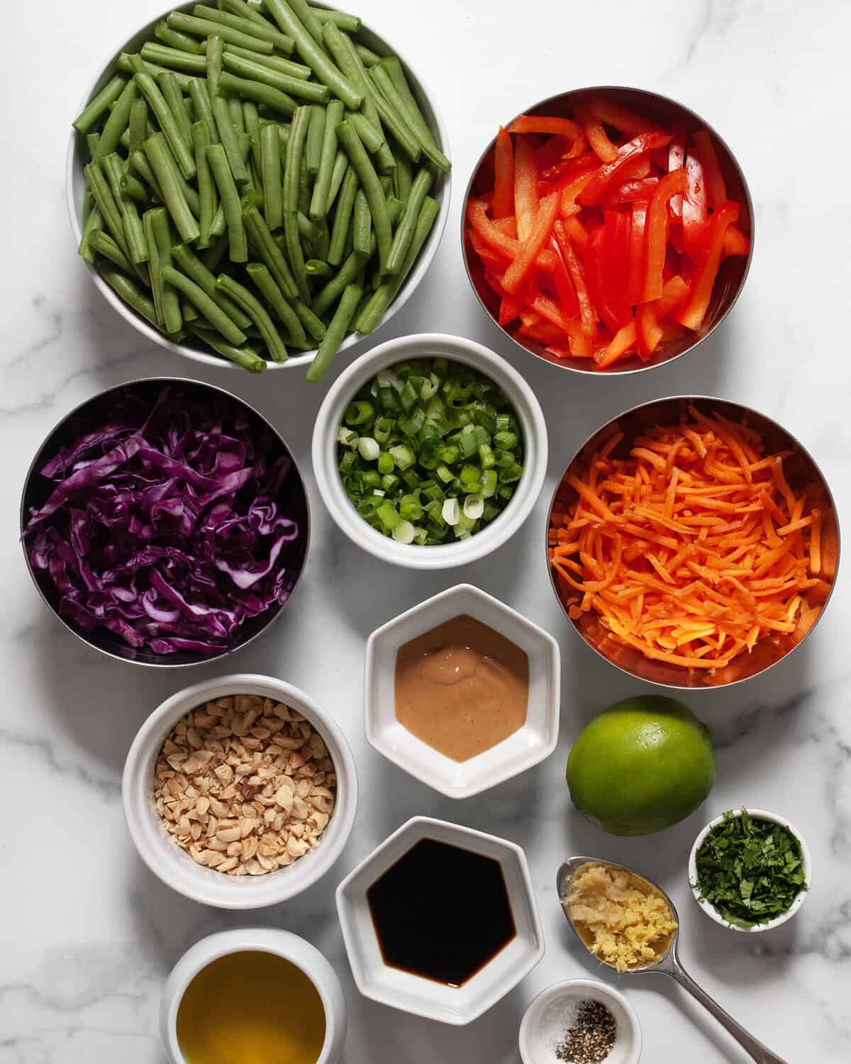 Ingredients including green beans, shredded carrots, shredded cabbage, bell peppers, scallions, cilantro, ginger, garlic, peanut butter, lime, salt, pepper and oil.