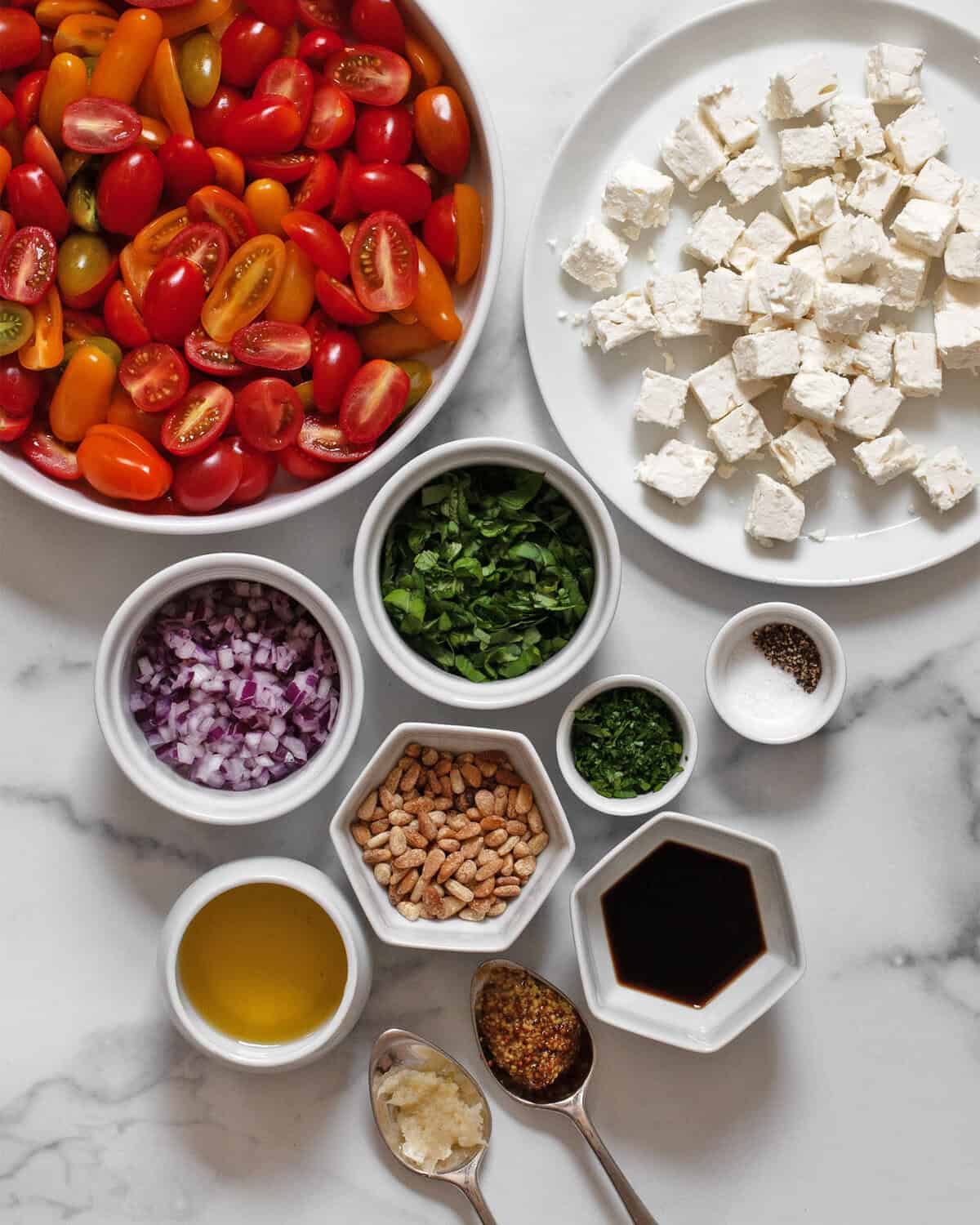 Ingredients including halved cherry tomatoes, feta, red onions, basil, parsley, balsamic vinegar, olive oil, garlic, mustard, salt and pepper.