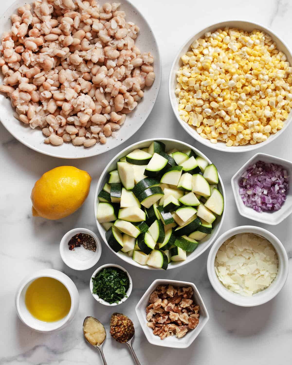 Ingredients including white beans, corn kernels, diced zucchini, red onions, lemon, walnuts, olive oil, shaved pecorino, garlic, mustard, salt, pepper and parsley.